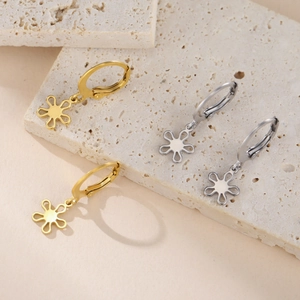 Détail de boucles d'oreilles créoles or et argent avec pendentifs fleurs sur pierre beige