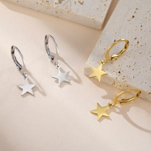 Close-up of minimalist gold and silver star earrings on a textured stone display