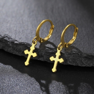 Gros plan détaillé de créoles en acier doré avec pendentifs croix sur une base de pierre