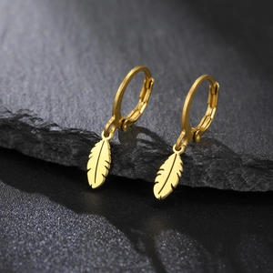 Détail macro de boucles d'oreilles créoles avec pendentifs plumes dorés sur roche noire