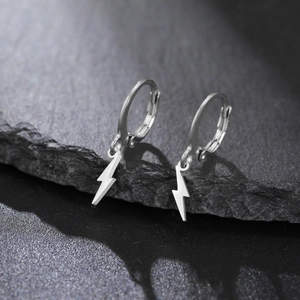 Gros plan de boucles d'oreilles créoles avec pendentif éclair argenté sur pierre sombre