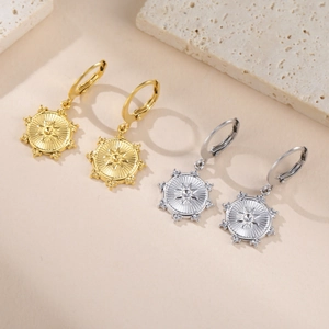 Detalle de aros dorados y plateados con colgante de estrella solar sobre piedra