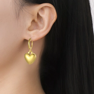 Primer plano de pendientes de corazón en oro de 18k llevados por una modelo en estudio