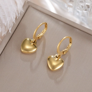 Vista macro detallada de pendientes de corazón bañados en oro 18K sobre bandeja blanca