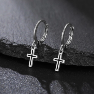 Détail macro de boucles d'oreilles créoles en acier avec pendentifs croix sur roche