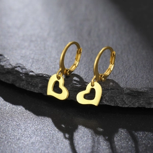Détail de créoles dorées avec pendentif cœur sur un fond de pierre noire texturée