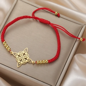Close-up of red braided rope bracelet with golden Celtic knot charm and beads