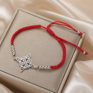 Detail of red braided cord bracelet with a silver Celtic knot charm and metal beads