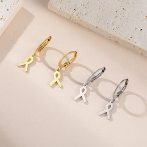Détail des créoles avec pendentifs ruban en or et argent sur un support en pierre
