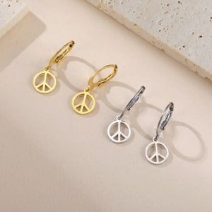 Détail de boucles d'oreilles créoles avec pendentif peace and love dorées et argentées