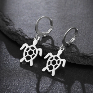 Boucles d'oreilles tortue en argent poli présentées sur un fond de pierre texturée noire