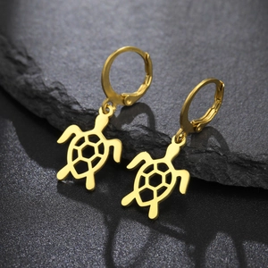 Détail de boucles d'oreilles tortue dorées avec découpes hexagonales sur fond de roche