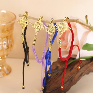 Detail of four colorful woven cord bracelets featuring golden Celtic knot charms on a branch