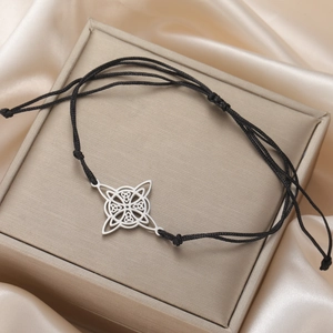 Detail of Celtic knot pendant on adjustable black woven cord bracelet with satin background