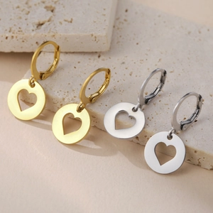 Détail de boucles d'oreilles cœur dorées et argentées sur fond de pierre beige naturel