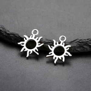 Pair of sun-shaped 18K gold plated stainless steel pendants on a dark natural rock