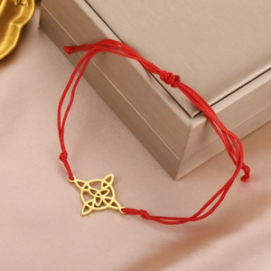 Detailed shot of red woven bracelet with golden Celtic knot charm on silk background