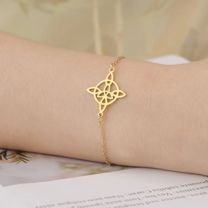 Detail of a gold plated stainless steel Celtic knot pendant bracelet worn on a wrist