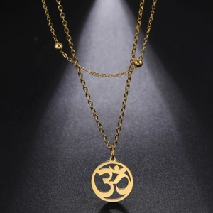 Macro detail of golden Om lotus pendant on double-layer beaded chain against grey background