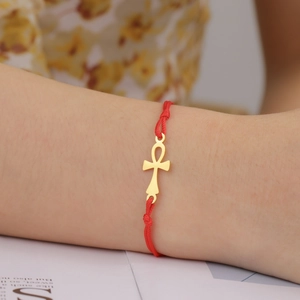 Close-up of golden Ankh pendant on a red braided cord bracelet worn on a wrist