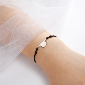 Close-up of minimalist graduation cap charm on black woven cord bracelet worn on wrist