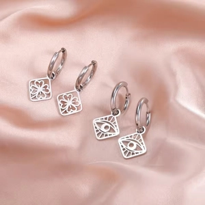 Detailed macro view of silver steel clover and evil eye hollow square charms on silk cloth
