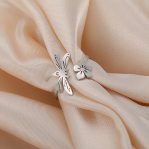 Detailed shot of stainless steel ring featuring dragonfly and flower on silk fabric