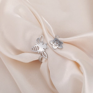 Detail of silver stainless steel bee and flower open ring on champagne silk fabric