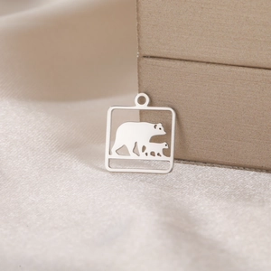 Detailed close-up of a square stainless steel bear charm on soft champagne satin fabric