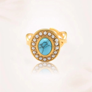 Detalle de anillo bohemio dorado con piedra turquesa ovalada y borde de perlas