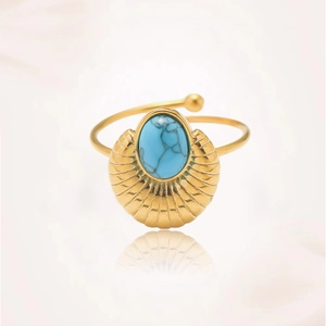 Detalle de un anillo dorado en forma de concha con una piedra turquesa ovalada