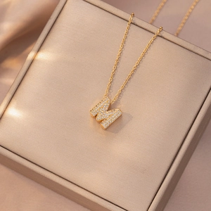 Elegante collana dorata con lettera M e zirconi luccicanti su sfondo di raso champagne