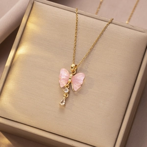 Detail van gouden vlinderketting met roze parelmoer vleugels en zirkoon op een juwelendoosje
