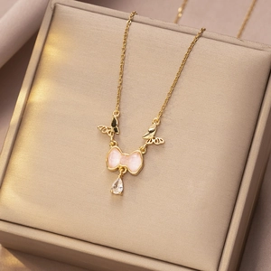 Detail van gouden vlinderketting met roze strik en kristallen druppel op satijn