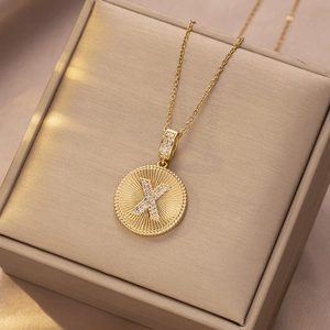 Nahaufnahme der goldenen Münzhalskette mit Zirkonia-Buchstabe X und Sonnenstrahl-Anhänger