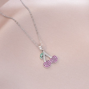 Detailed close-up of cherry pendant necklace with pink and green stones on silk fabric