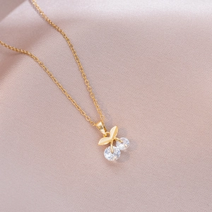 Macro shot of gold cherry pendant necklace with clear zircon stones on pink silk fabric