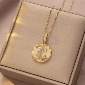Makroaufnahme einer goldenen Edelstahlkette mit rundem N-Anhänger und Zirkonia-Besatz