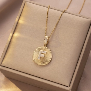 Detail der goldenen Halskette mit F-Anhänger und Zirkonia auf einer Schmuckbox