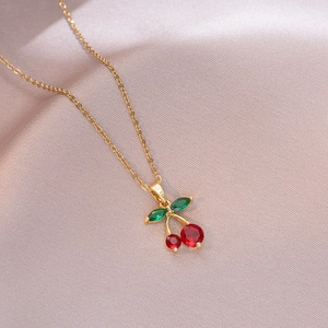 Close-up of golden cherry necklace with red round gems and green leaf-shaped stones