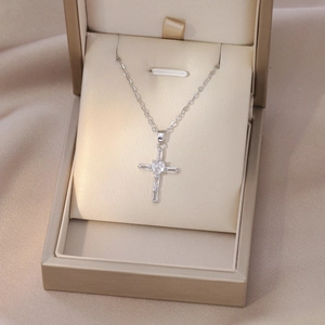 Detailed view of silver cross pendant with heart-shaped crystal on satin box
