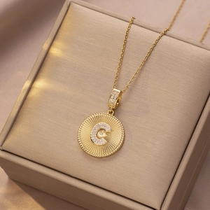 Detail der Goldkette mit Diamant-Buchstaben C und radialer Textur auf dem Anhänger