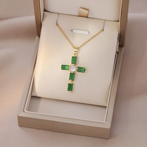 Detailed close-up of gold cross necklace with emerald-cut green zircons in a jewelry box