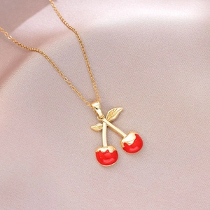 Detailed shot of a red cherry pendant with golden leaves on a gold chain necklace