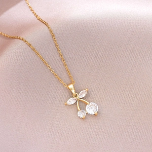 Detail of gold cherry necklace with sparkling zircon pendant on pink silk background