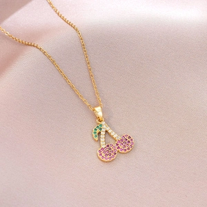 Macro shot of gold cherry necklace with pink and green pavé crystals on silk fabric