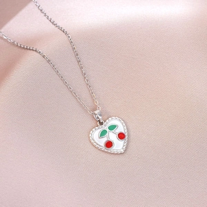 Close-up of heart-shaped cherry pendant necklace on soft pink satin fabric background