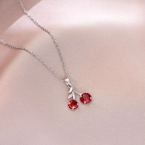 Close-up of cherry pendant necklace with red crystals and silver leaf on silk