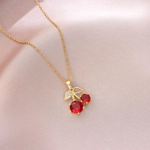 Close-up of cherry pendant with red gems and gold leaves on pink satin fabric