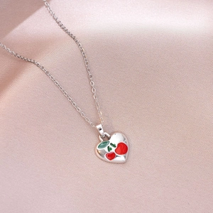 Detail of heart-shaped cherry pendant on silver chain over pink silk background